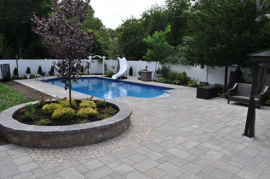 backyard patio with inground pool and small landscaped garden with trees and plants